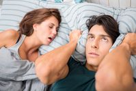 Imagen sobre el tema Mujer joven ronca junto a su pareja en la cama, quien está molesta y presiona la almohada sobre sus orejas